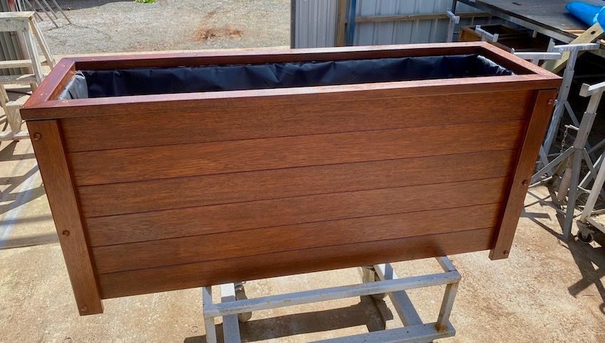 Timber planter box with a dark interior on a stand outdoors