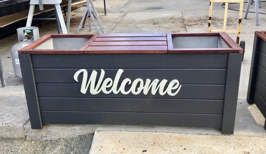 Dark grey timber planter box with white Welcome script on the front