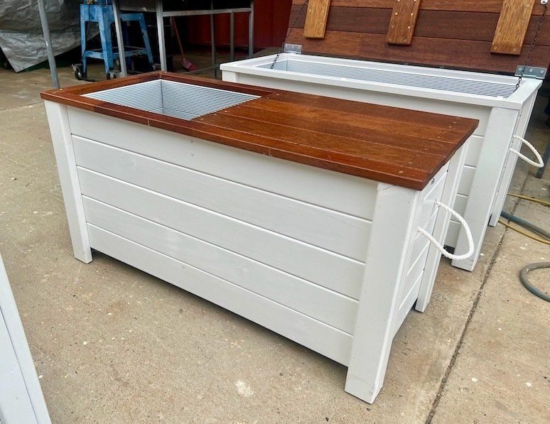 White timber raised garden beds with brown tops, one with a metal sink