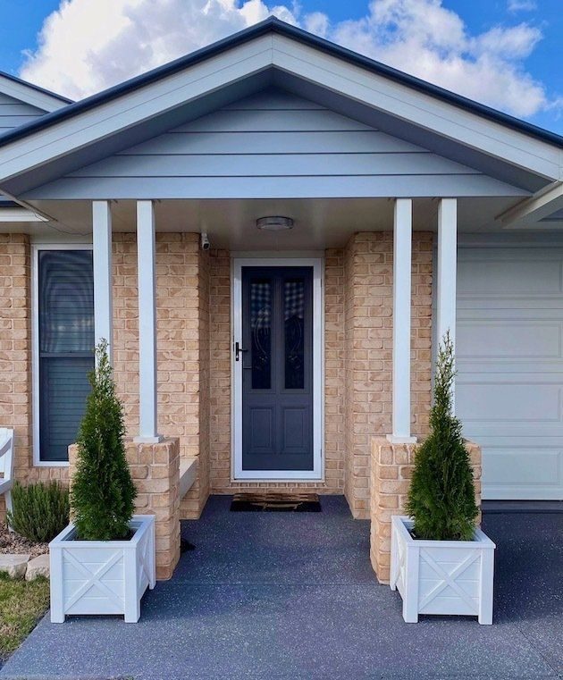 Front porch with a blue door, white columns and potted shrubs by the entrance