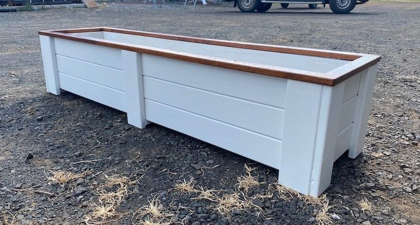 White timber outdoor bench with a brown top on gravel