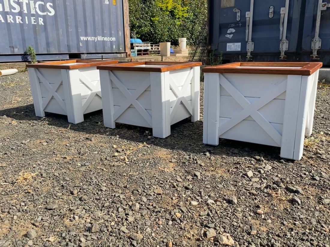 Three white outdoor planter boxes with timber tops on gravel