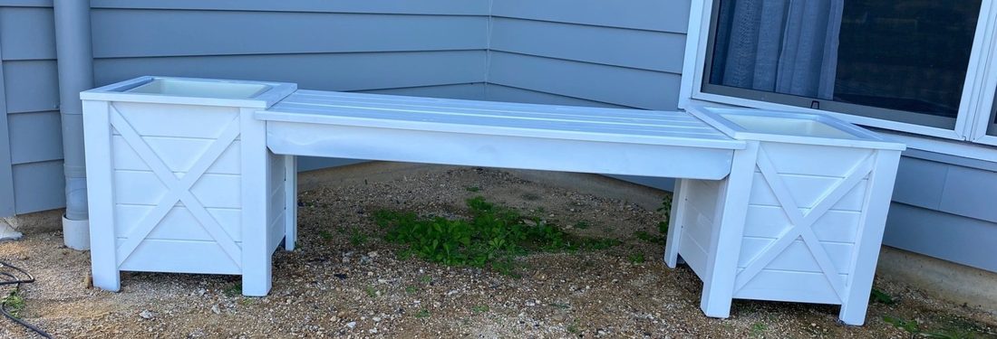 White timber bench between two white storage boxes against a house wall