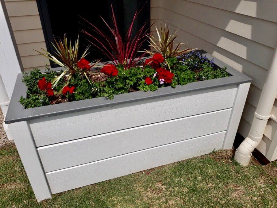 White planter box with red and green flowers beside a house wall
