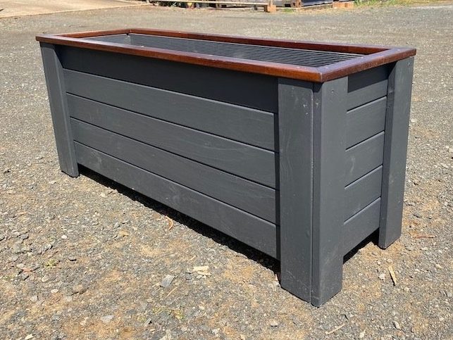 Charcoal-grey timber planter box with a brown top trim on gravel