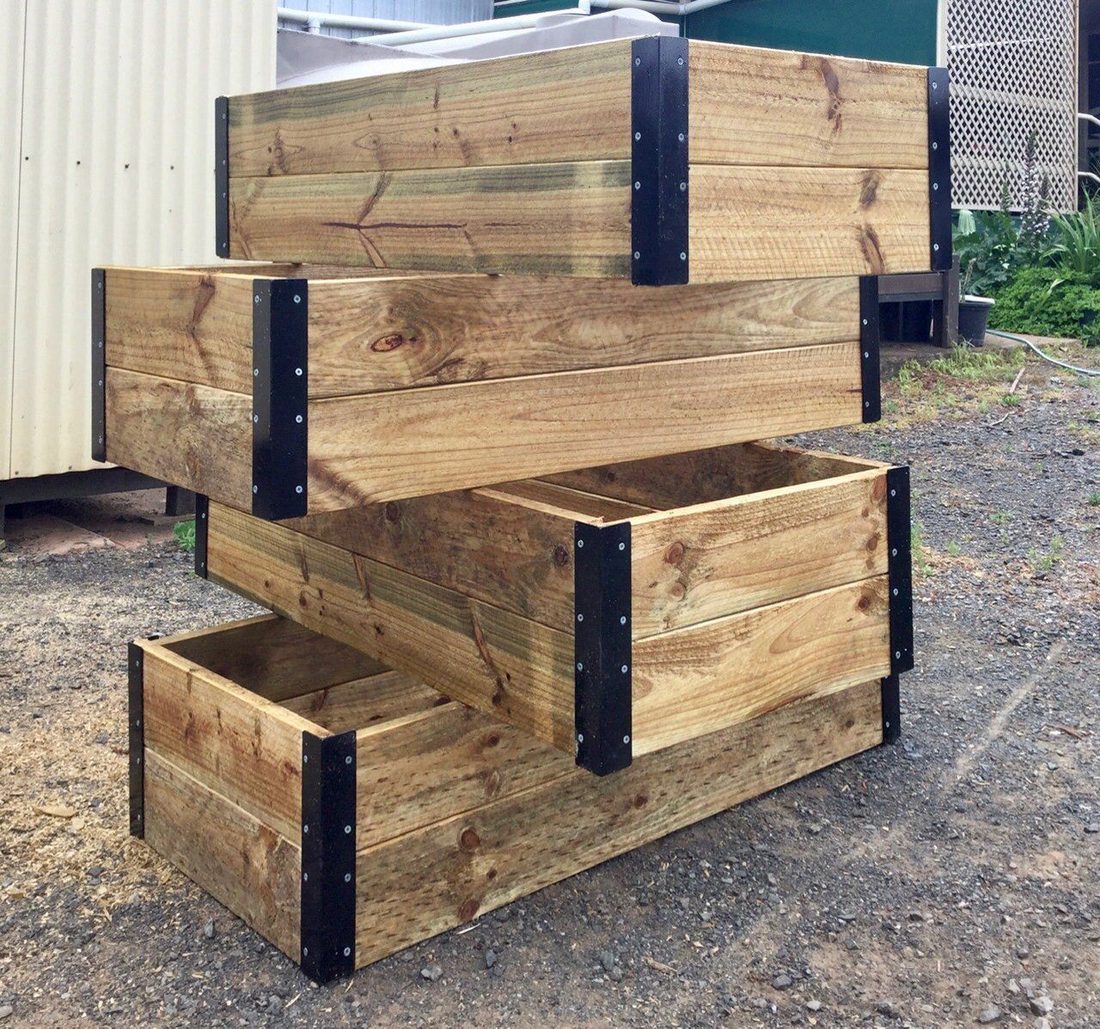 Stacked timber planter boxes outdoors with black metal corner brackets