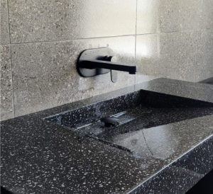 Modern black stone sink in newly renovated bathroom. Natural grey wall tiles fixed behind and above sink.