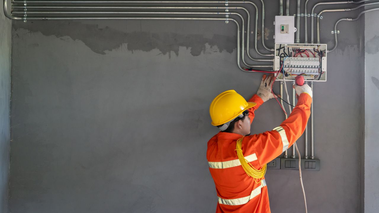 New Earth Electrics electrician wiring a switchboard in hi-vis