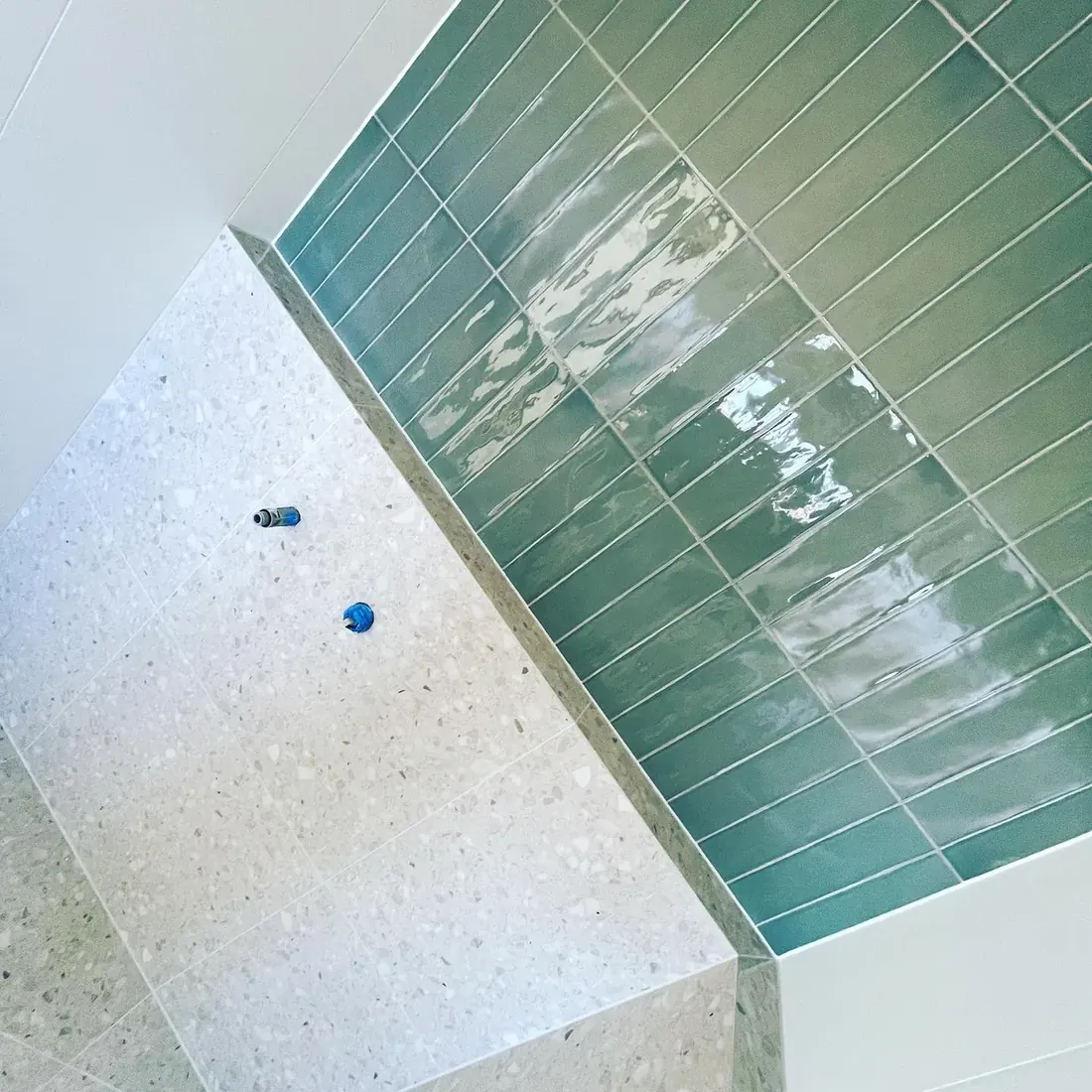 Glossy green subway tile paired with terrazzo flooring