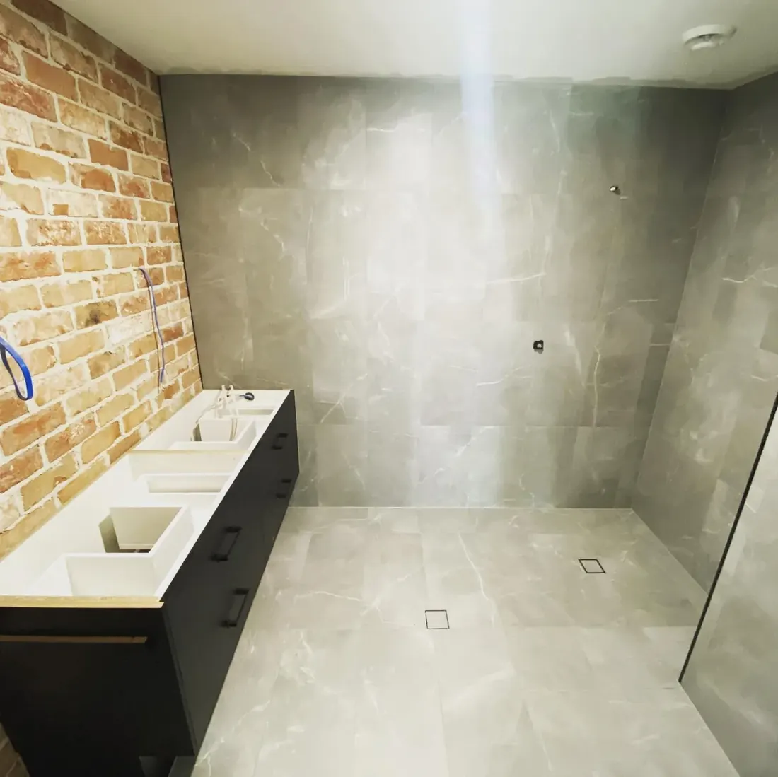 Large bathroom with grey marble-look wall tile and a recycled-brick feature wall
