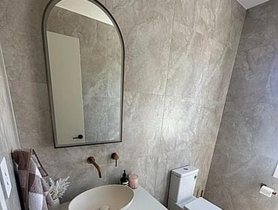 Arched mirror feature bathroom with stone-tile walls