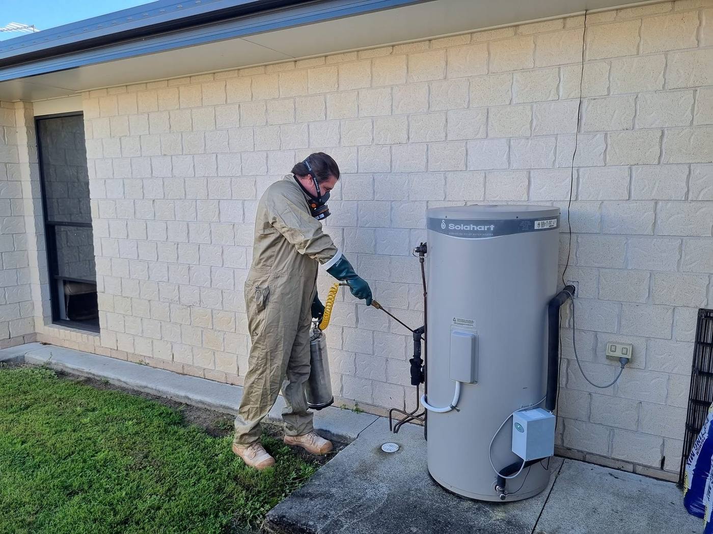 Technician applying pest treatment around a hot water system